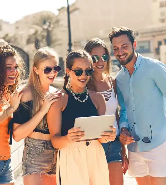 Five happy friends standing in front of a tablet planning a trip together